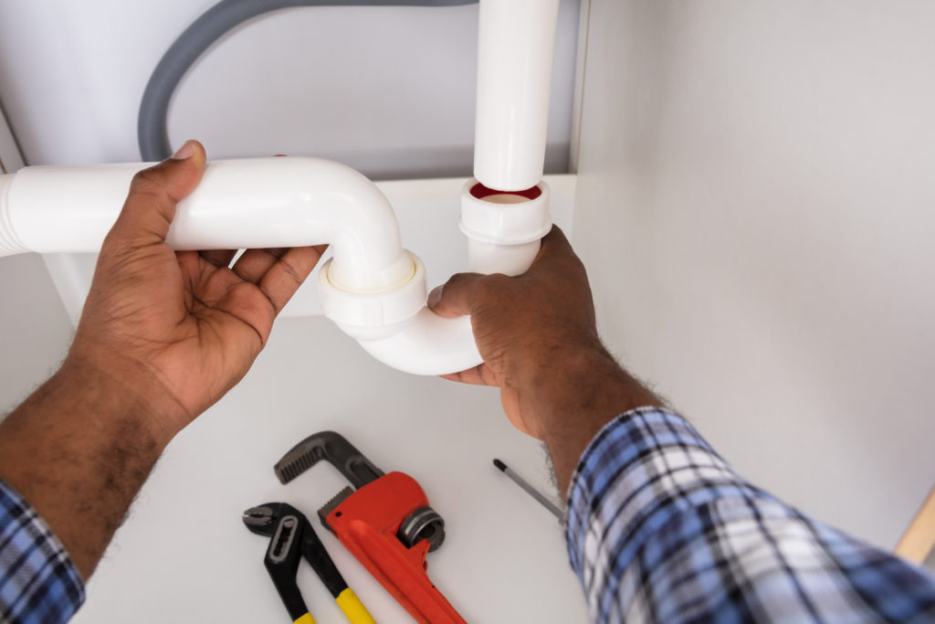 Plumber repairing the drain trap under a sink