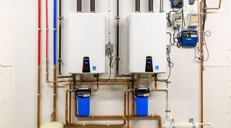 Two tankless water heaters installed side by side with plumbing and filters